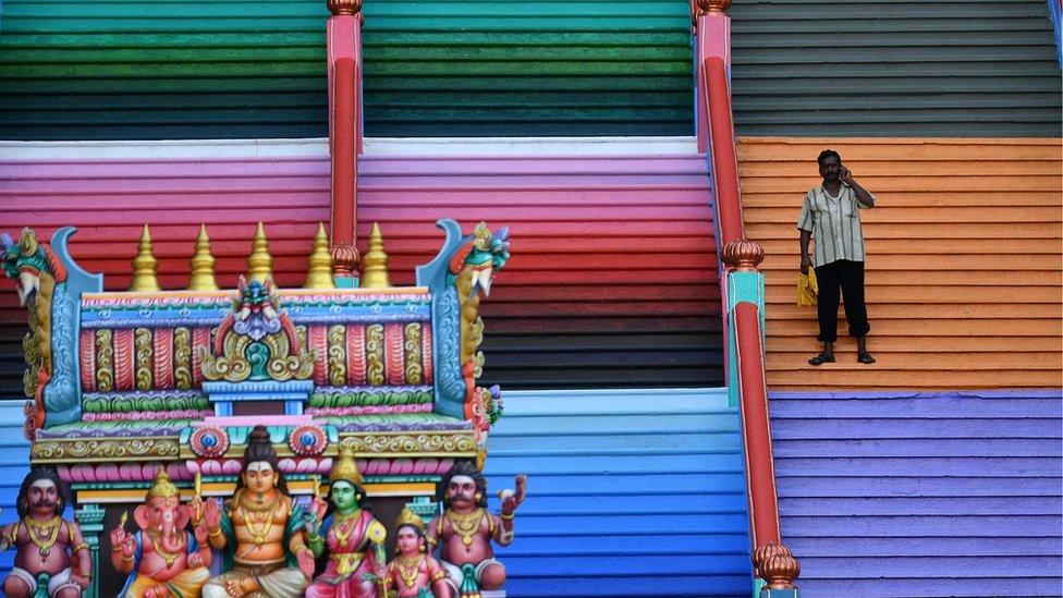 A man speaks on his phone in front of the staircase at Malaysia's Batu Caves complex