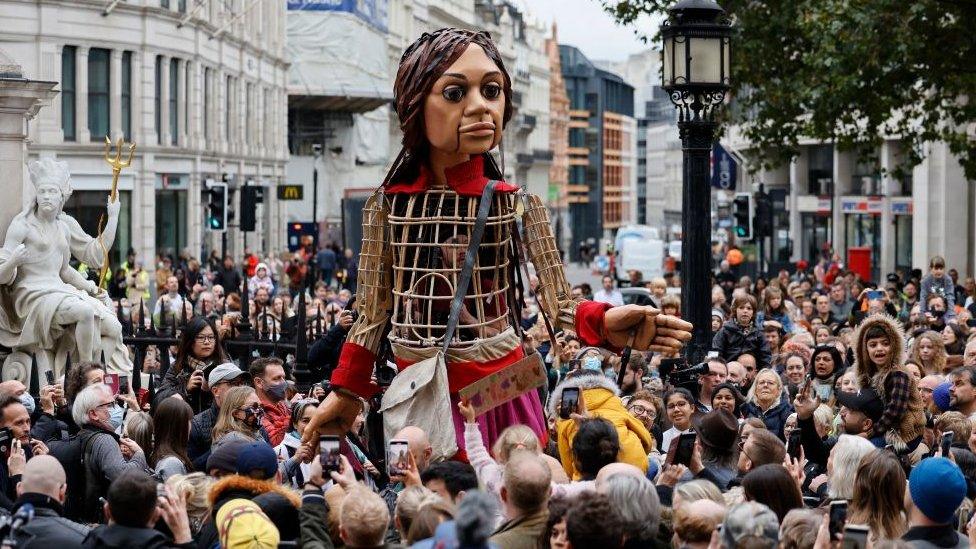 Little Amal in crowd, large puppet