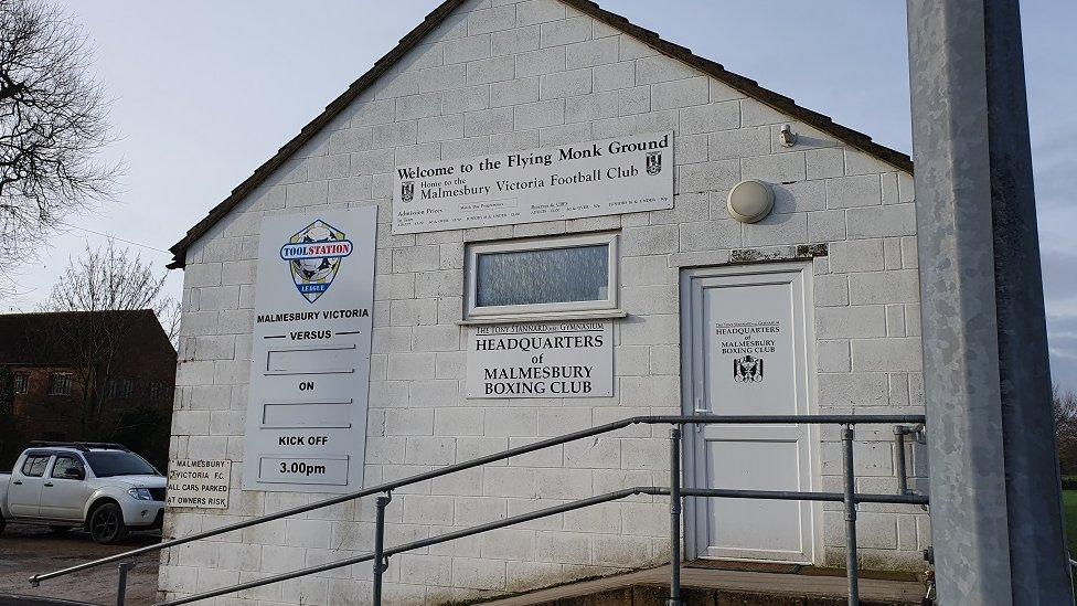 Plain white painted breezeblock building with sign on saying it is the football ground