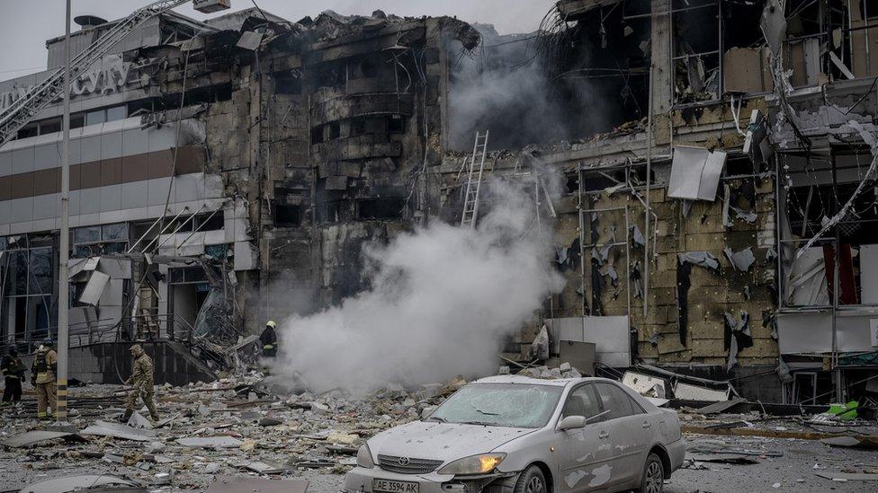 A building in Dnipro with a bomb crater with smoke emerging from it