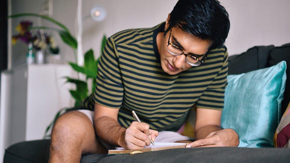 Man writing in a diary sitting on a sofa