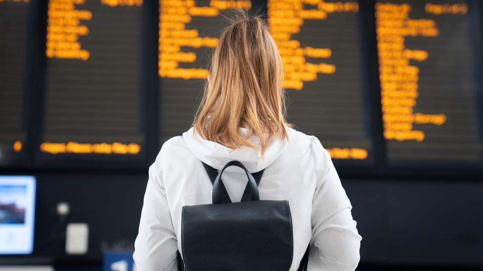 Woman stands in front of train notice board