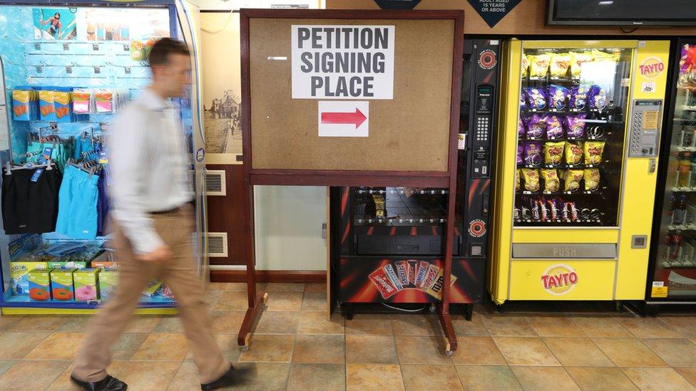 A man walks past signage for a recall petition at the Joey Dunlop Leisure Centre in Ballymoney