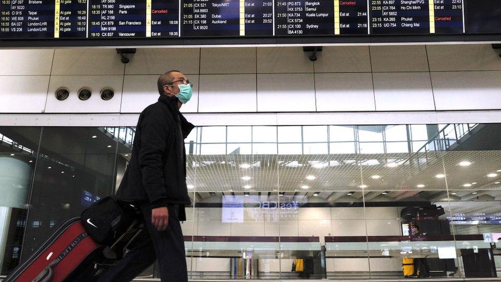 Aman wearing a mask pulls suitcase as he walks past a flight information display board