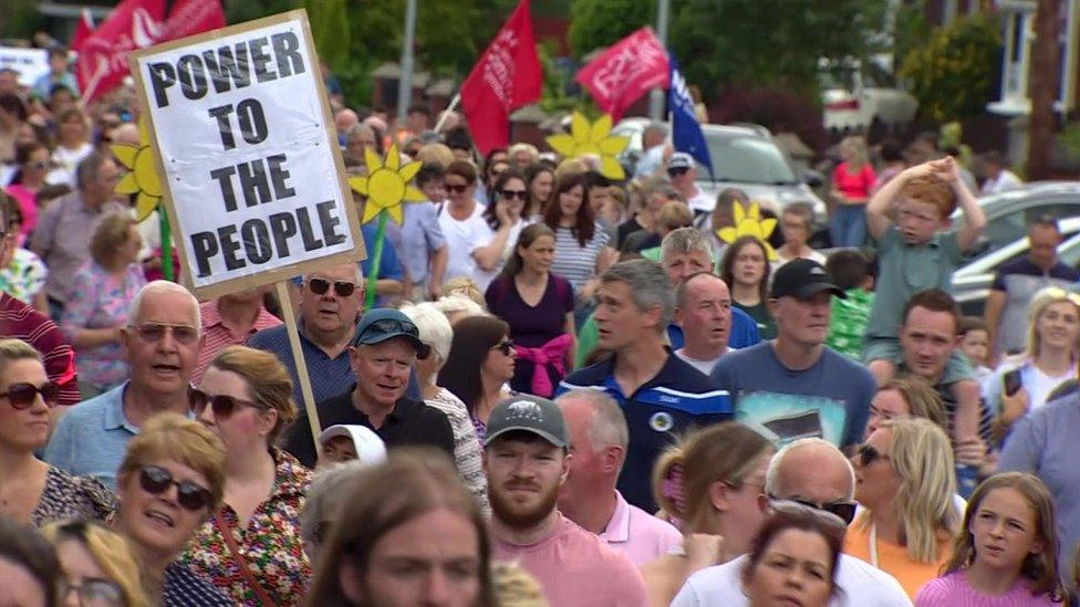 Protesters marching towards Daisy Hill Hospital, with one holding a placard that reads: POWER TO THE PEOPLE