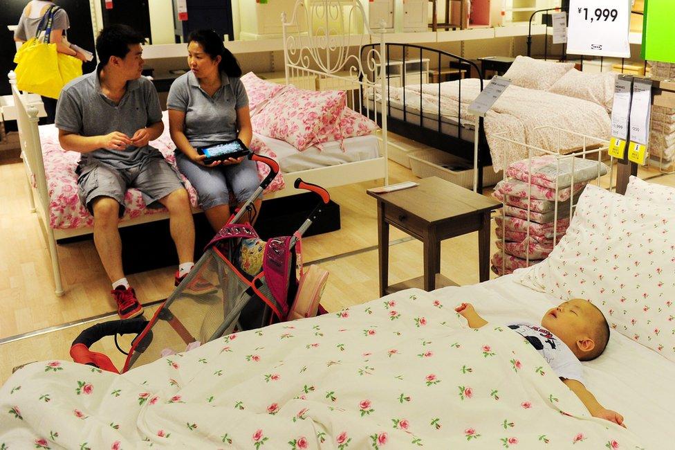 A young Chinese couple wait as their baby sleeps on a display bed, as they shop at an Ikea furniture store in Beijing on 15 August 2011