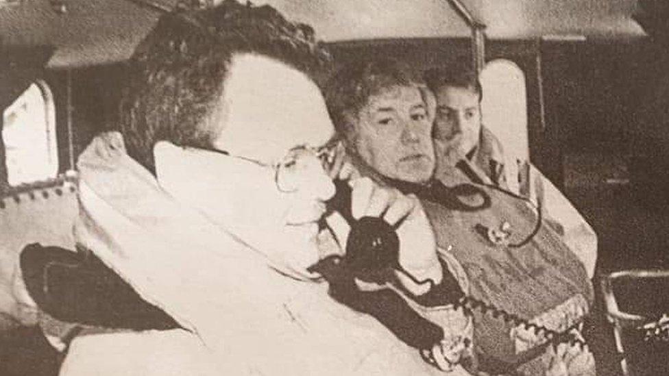 Black and white picture of three men in a lifeboat cabin. Geoff, the nearest to camera, is on the phone