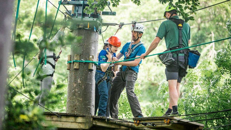 Oliver Vosyey takes part in a zip-line across a wooden bridge