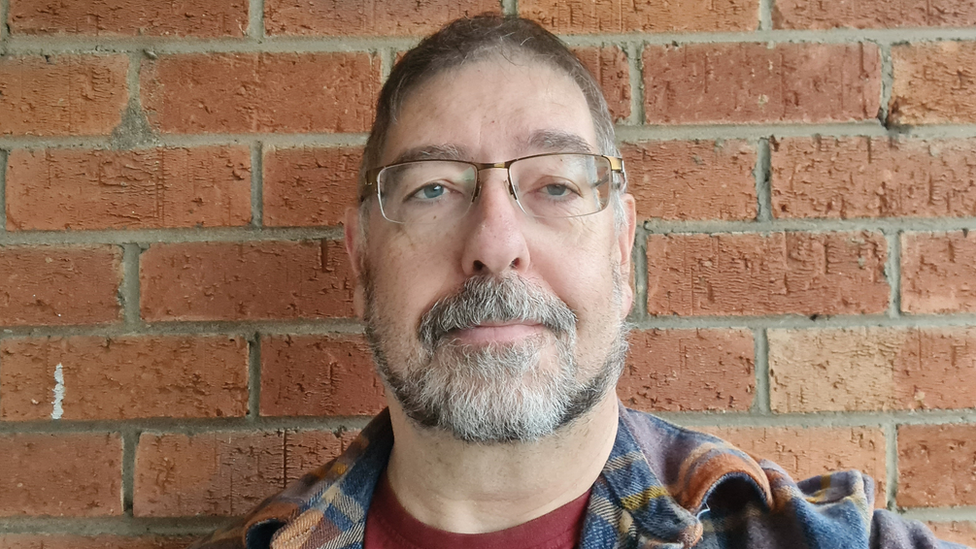 Chris Robinson stands in front of a red brick wall