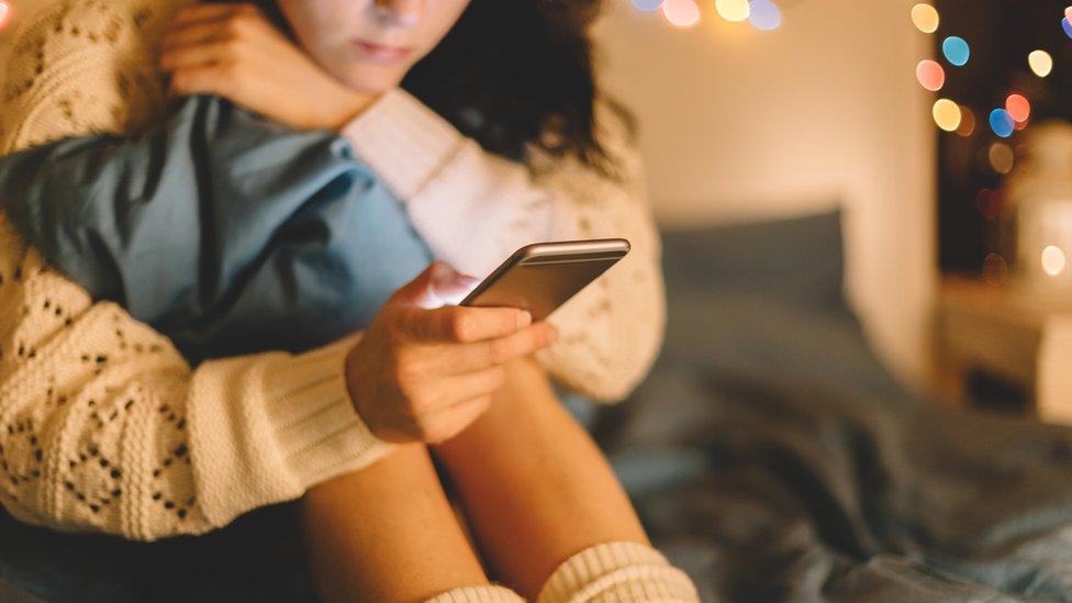 A young girl looks at her phone in this staged photo