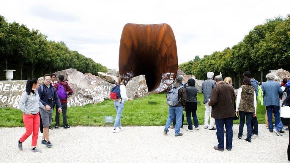 The public look at a vandalised steel sculpture by Anish Kapoor