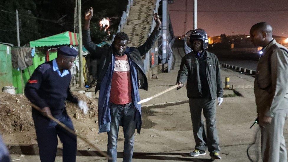 Kenyan police officers interrogate and conduct a body search on a man (C), whom they found walking at night as they patrolled