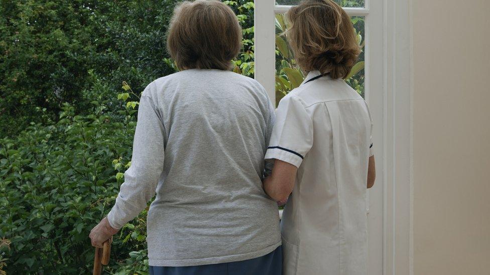 A nurse supporting an elderly woman