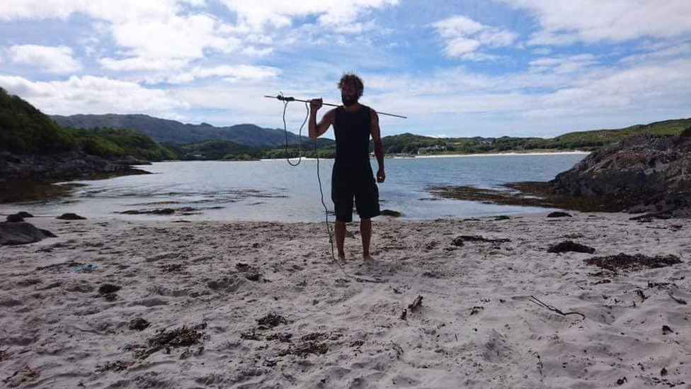 Chris on a beach with a fishing spear