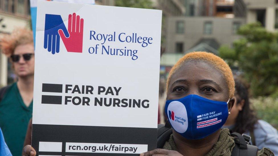 Nurse wearing a facemask and holding a banner that reads "fair pay for nursing"