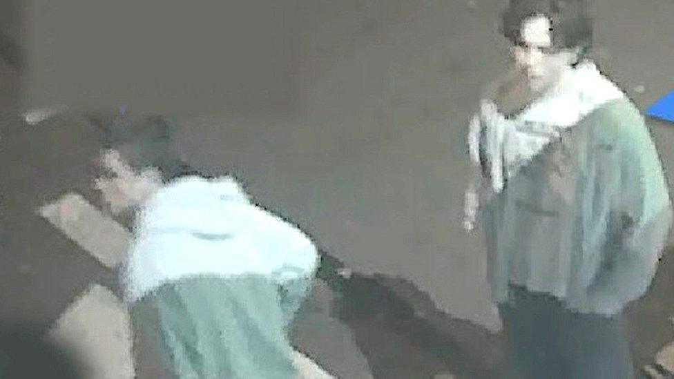 CCTV of two men standing in the street wearing pale hoodies and dark trousers