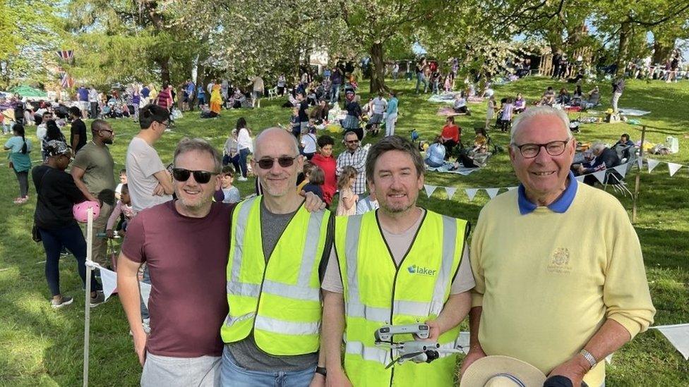 Organising committee Secretary Nick Baker, Vice Chair Brian Bates, Chairman Stephen Sangster and David Horder in front of picnickers in the park.