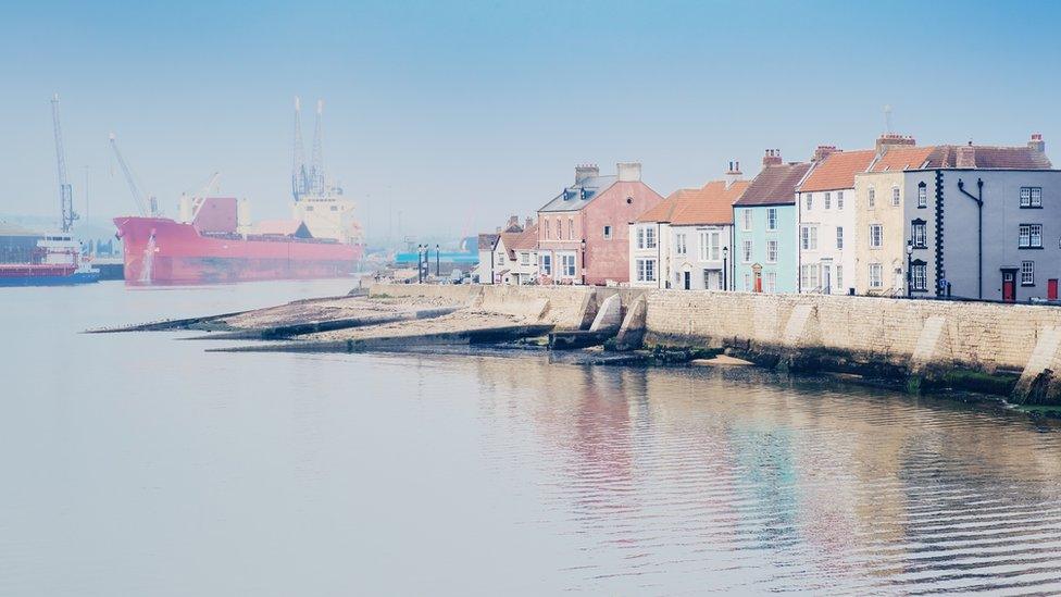 Misty view of houses next to sea wall and ship in distance