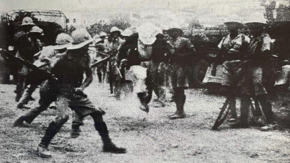 A black and white photo of rows of soldiers holding batons ready to swing and