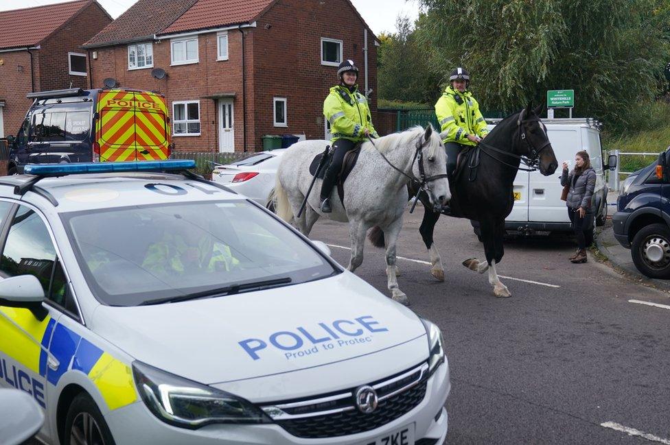 Police on horses ride past police car at the scene