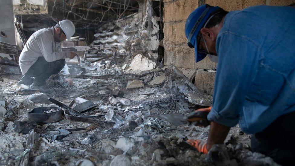 Israeli archaeologists inspect charred debris on the floor of a house in southern Israel that was set on fire during Hamas's attack on 7 October