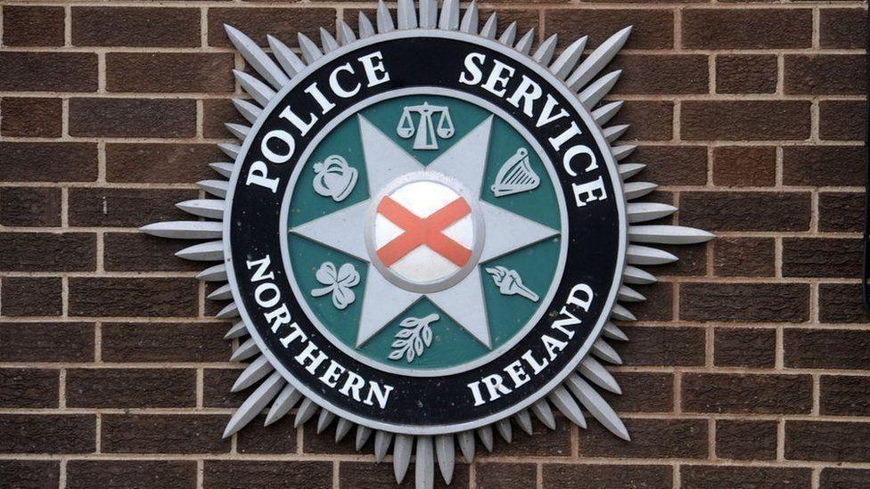 A PSNI crest hangs on a brick wall