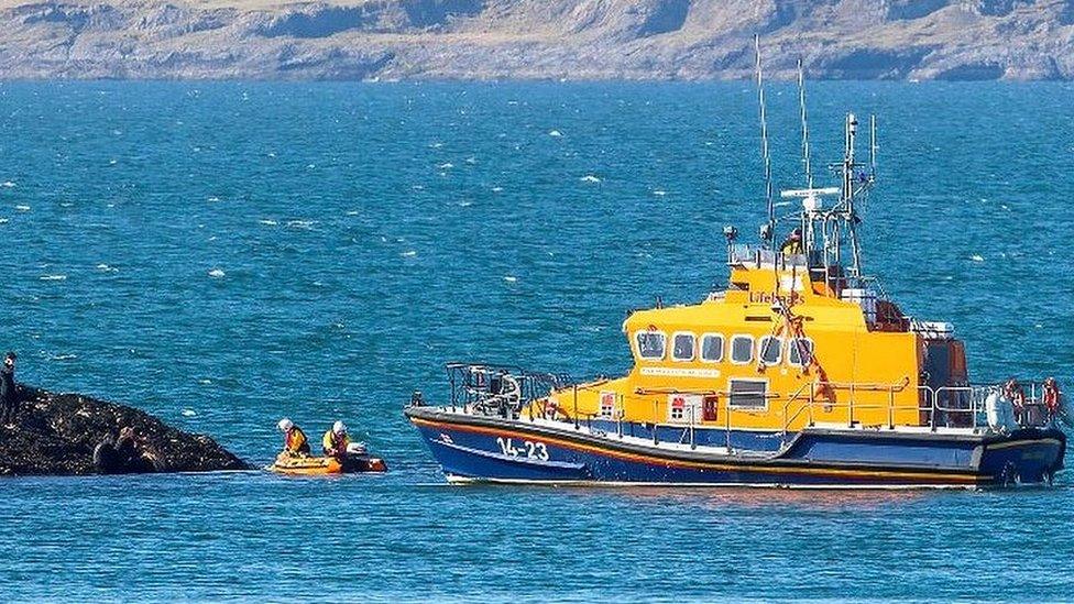 Yellow lifeboat in water carrying out a rescue with a larger boat behind supporting