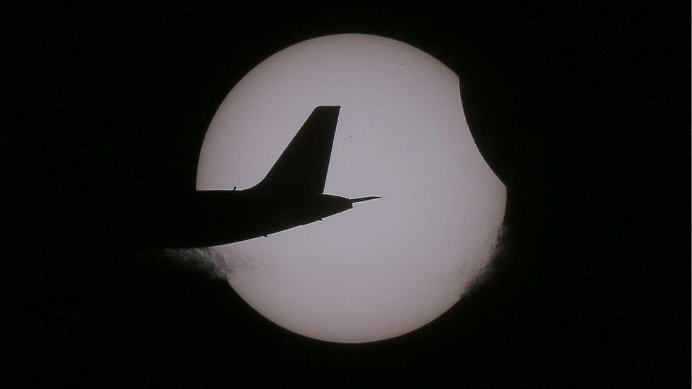 A plane is seen passing in front of a partial eclipse over Taguig City in the Philippines.