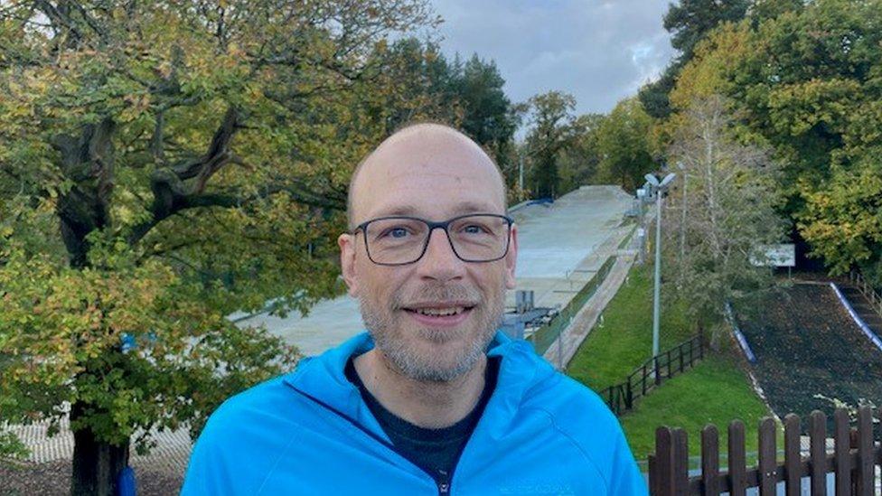 A man in glasses standing in front of a ski slope