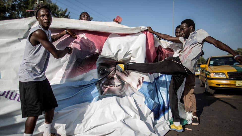 A group of Men kick a billboard poster of President Yahya Jammeh.