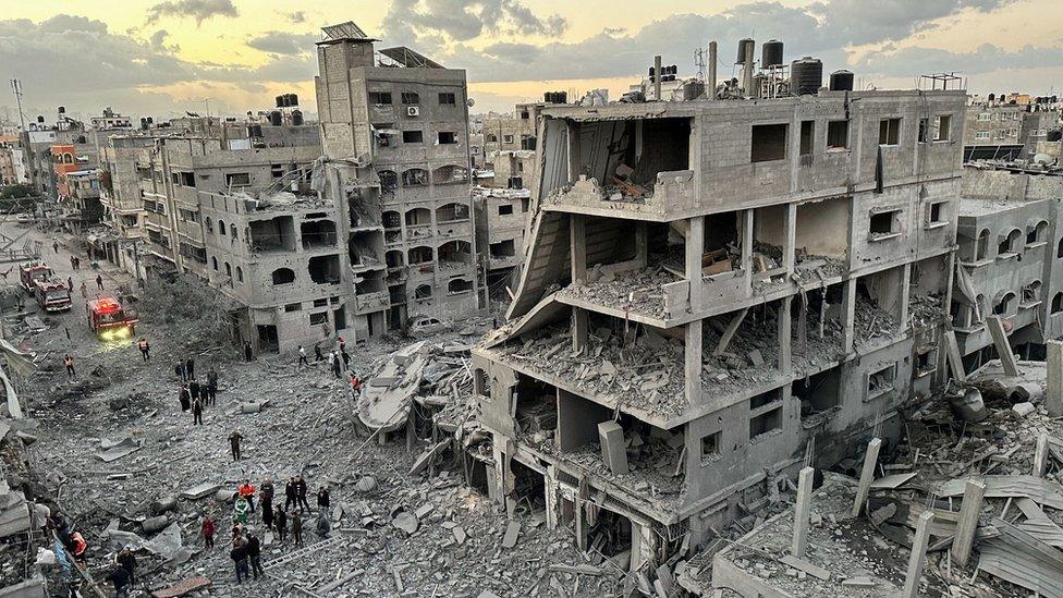 Palestinians walk past destroyed buildings in Jabalia refugee camp, in the north of the Gaza Strip (21 November 2023)