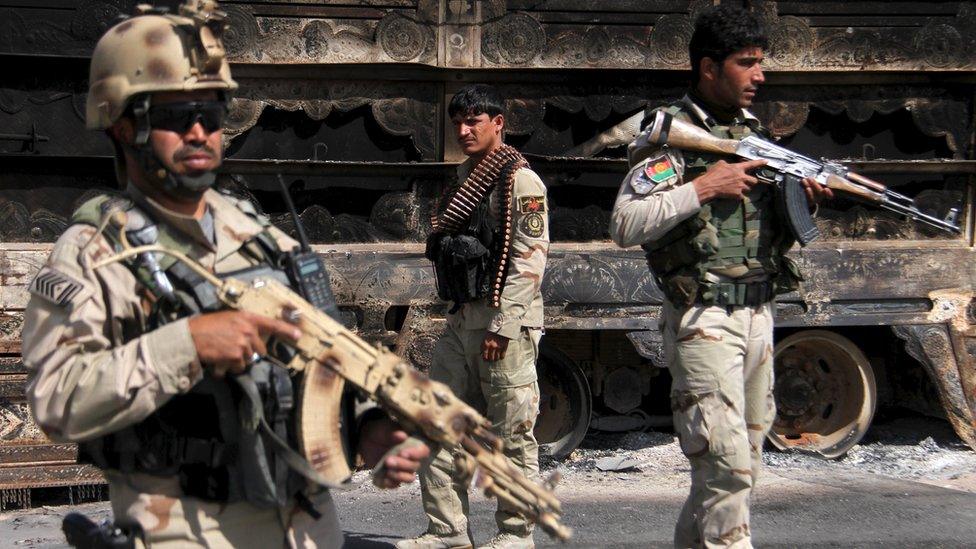 Afghan security forces keep watch in front of a vehicle which was set on fire on the Kabul-Kandahar highway after fighting between government forces and Taliban militants in Ghazni, Afghanistan October 14, 2015