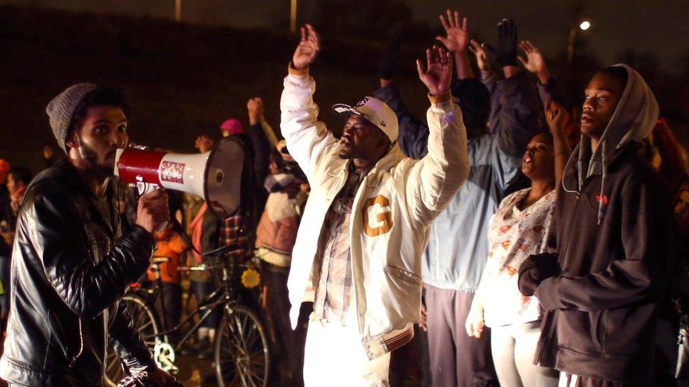 Protesters stand with their hands in the air