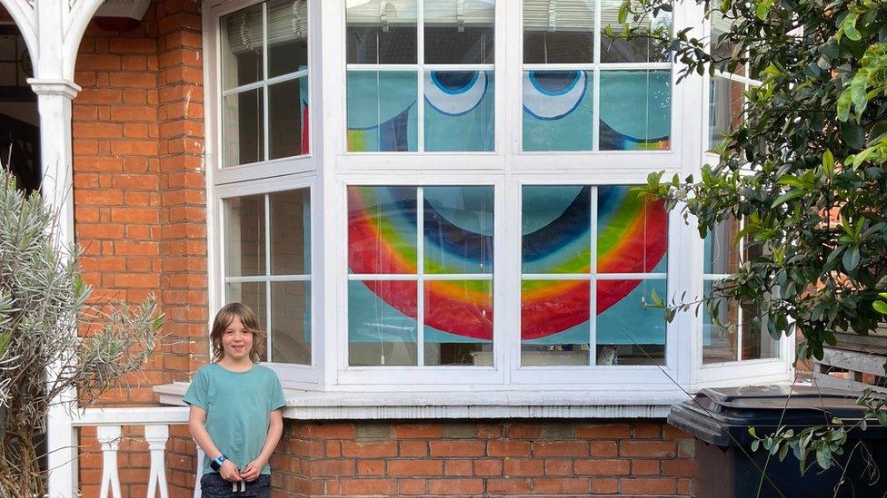 mateo-stands-outside-house-with-massive-window-showing-big-rainbow-smiley-face