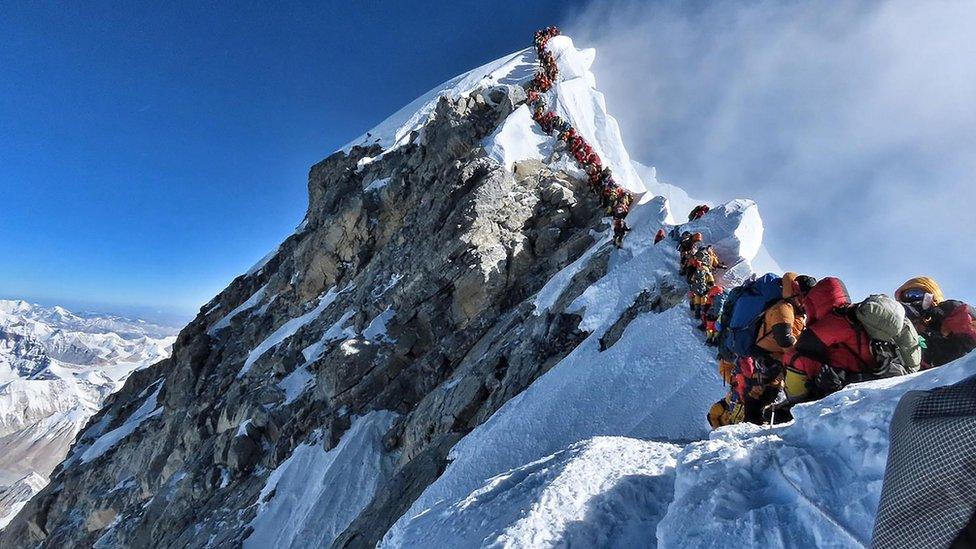 Heavy traffic of mountain climbers lining up to stand at the summit of Mount Everest.