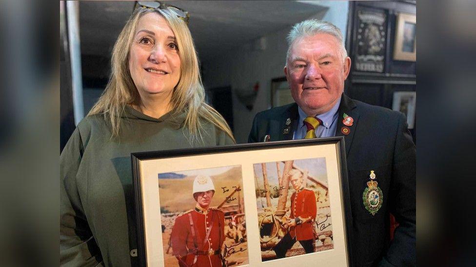 Donna Haslam and Mike Hall hold up a framed set of two photographs of Sir Michael Caine dressed in red military dress on the set of 1964 film Zulu.