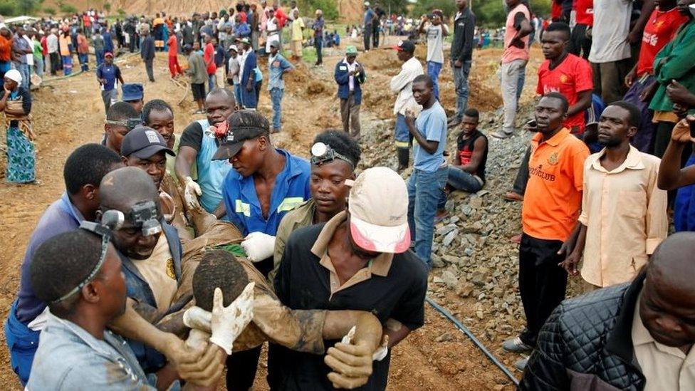 ten men carrying one rescued miner past a crowd of onlookers