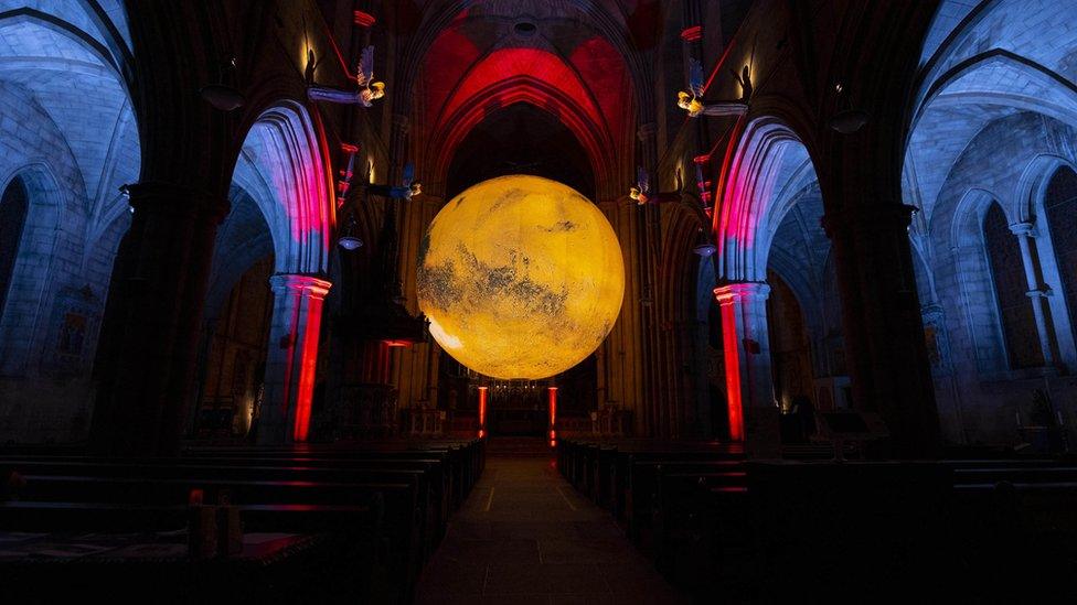 A big art installation in a dark glowing room that displays planet Mars