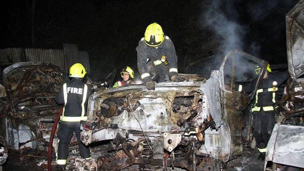 Firefighters on top of burnt cars as they try to put out a fire