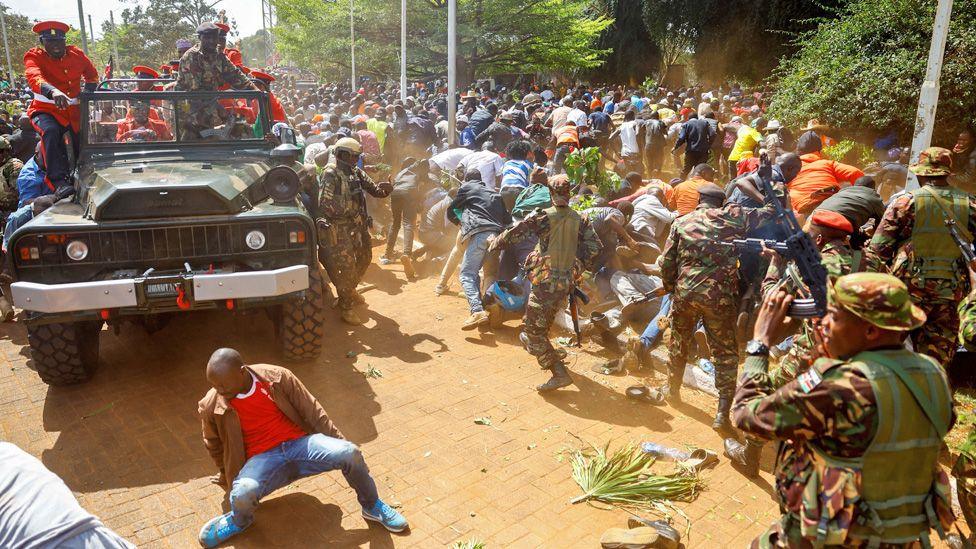 Crowds scatter, some falling to the dusty ground, as the security forces try to disperse them as the vehicle carrying Raila Odinga's body arrives at a stadium.