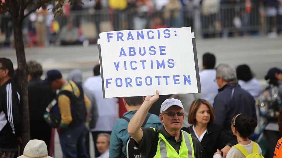 Activist with sign denouncing the church's alleged lack of response to the abuse of children by clergy