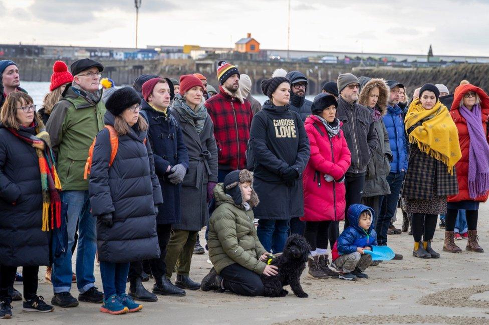 A crowd of people gather on a beach to protest