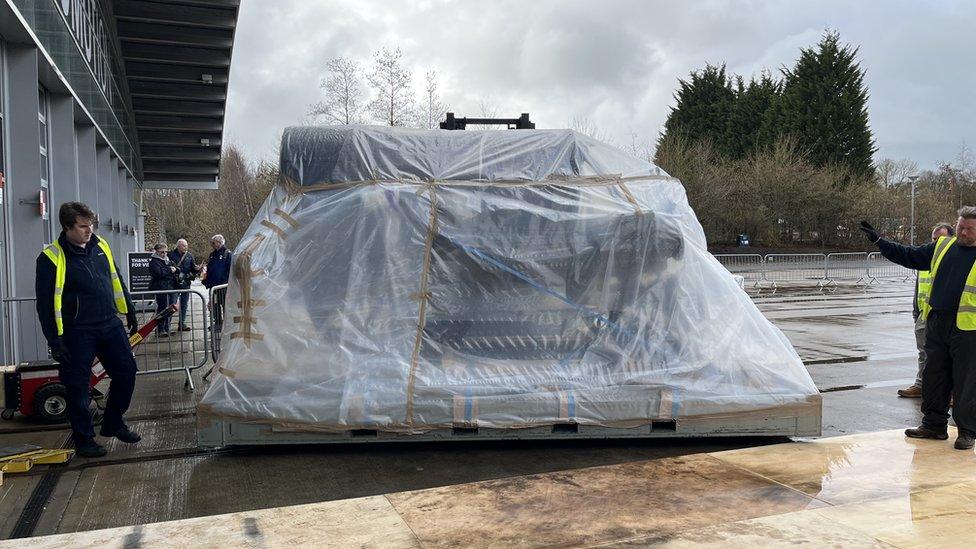 Rocket all wrapped up in plastic sheets being carried by a forklift