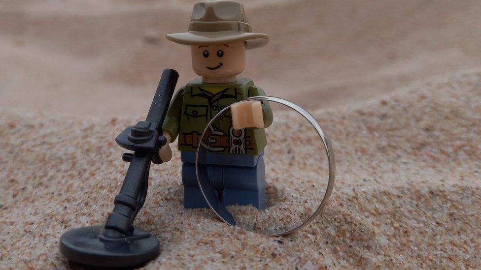 Lego man holding ring and metal detector