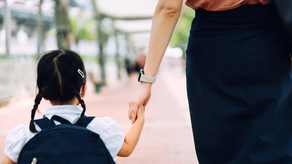 Rear view of young Asian mother taking her little daughter to school