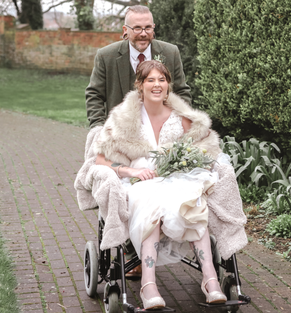 Richard Odams pushes bride Heather in a wheelchair