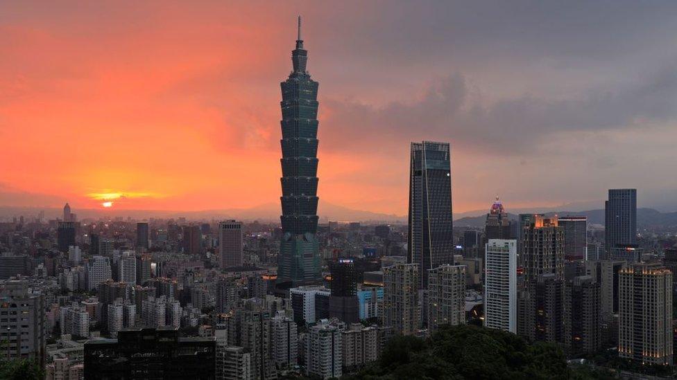 still shows taipei at sunset with lots of tall buildings and large hills and mountains in the background