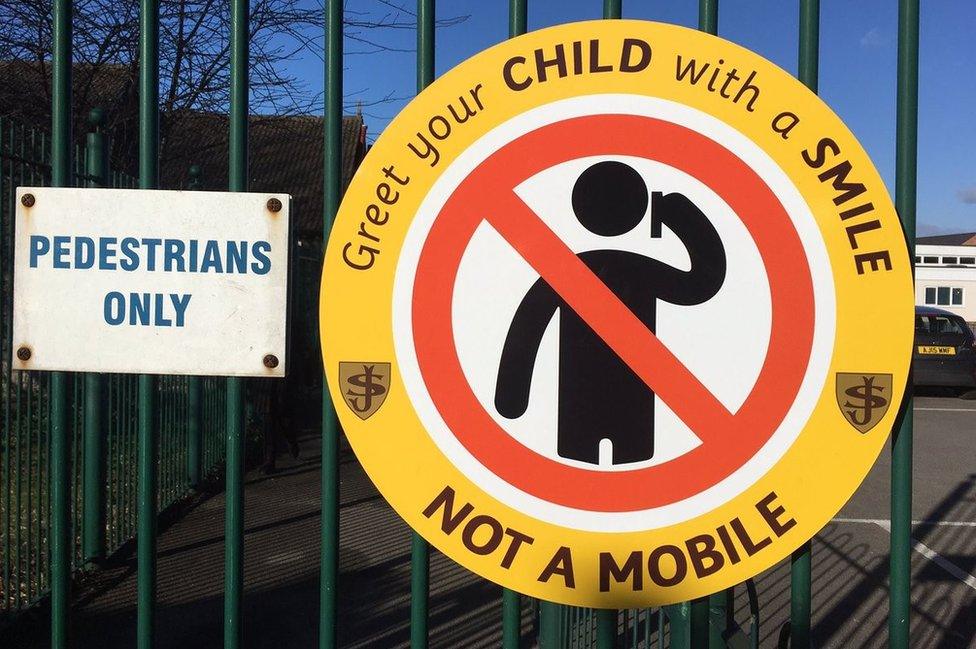 A sign at the school gates, which says: "Greet your child with a smile not a mobile"