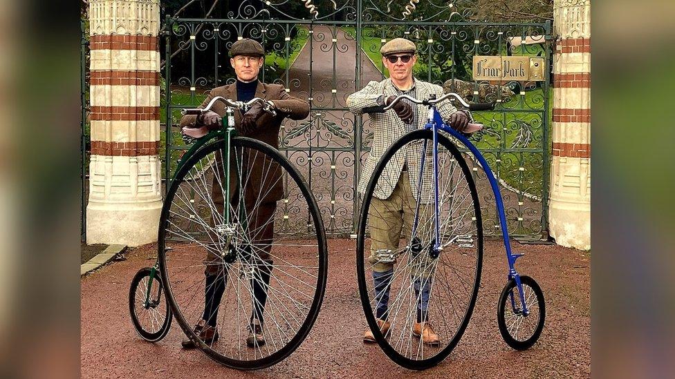 two men standing by penny farthings