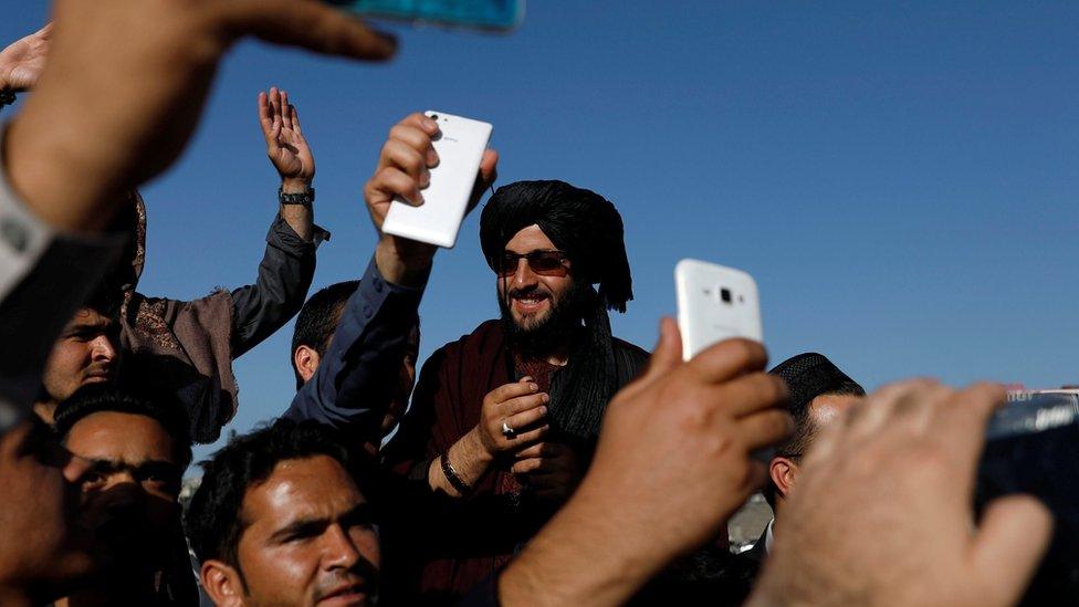 Afghans take pictures with a militant in Kabul